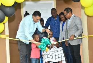 Prime Minister, the Most. Hon. Andrew Holness (left), cuts the ribbon to hand over a three-bedroom house, built under the New Social Housing Programme (NSHP), to beneficiary, Beverley Espeut (in wheelchair), during a handover ceremony held in Fort George, Annotto Bay, St. Mary, on December 21.  Looking on are relatives and friends of Miss Espeut; Permanent Secretary in the Ministry of Economic Growth and Job Creation, Arlene Williams (second right) and Member of Parliament for St. Mary South Eastern,  Dr. the Hon. Norman Dunn.