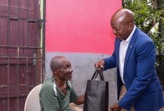 Minister of Labour & Social Security, Hon. Pearnel Charles Jr, presents a food package to 69-year-old Eli Powell, during a visit to his home on Henley Road, Kingston 11, on Thursday (December 21). Mr. Powell, who is blind, is a beneficiary of the Programme for Advancement Through Health and Education (PATH) and the National Council for Senior Citizens (NCSC).

