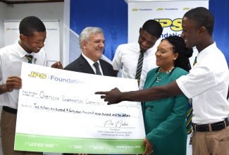 Deputy Chief Education Officer, Curriculum and Services Division, Ministry of Education and Youth, Dr. Clover Hamilton-Flowers (second right), looks at a symbolic cheque valued at more than $2.6 million, representing grant funding by the Jamaica Public Service Company (JPS) towards Caribbean Secondary Education Certificate (CSEC) Industrial Technology (Electrical) examinations for academic year 2023/2024. She is joined by (from left) Kingston High School student, Bently Mills; Clarendon College student, Austin Wright, and Brandon Levy also of Kingston High. Chairman of JPS, Damian Obiglio (second left), made the presentation during a ceremony held at the company’s offices in New Kingston on December 5.