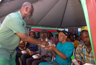 Minister of Local Government and Community Development, Hon. Desmond McKenzie (left), hands a meal to an elderly resident during Wednesday’s (December 20) annual West Kingston Senior Citizens’ Treat held at the Tivoli Gardens Community Centre in Kingston. 

