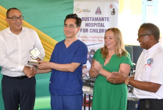 Health and Wellness Minister, Dr. the Hon. Christopher Tufton (left), presents a plaque to Professor of Cardiac Surgery, Chain of Hope, Victor Tsang (second left), in recognition of his work with the Bustamante Hospital for Children. Applauding are Chief Executive Officer, Chain of Hope, Emma Scanlan (second right); and Chief Executive Officer, Bustamante Hospital for Children, Anthony Wood. Occasion was a function held at the hospital in Kingston on November 30, to recognise Chain of Hope’s 20th year of cardiac care support at the facility.  Ten children with heart conditions benefited from the charity’s latest mission from November 27 to December 1.