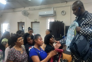 Founder of the Power of God Ministries International (PGMI), Prophet Roydel Rowe (right), hands over school bags to parents at the church, in Mandeville, Manchester, recently.