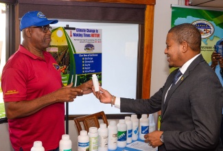 Minister of Agriculture, Fisheries and Mining, Hon. Floyd Green (right), looks at a product to promote plant health during a visit to the St. Jago Farm and Hardware Supplies booth at the World Soil Day Seminar on Tuesday (December 5), at the Jamaica Conference Centre, downtown Kingston. Highlighting the benefits of the solution is Product Development Officer at St. Jago Farm and Hardware Supplies, Cassidy Beckford.