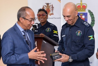 National Security Minister, Hon. Dr. Horace Chang (left), and Commissioner of Police, Major General Antony Anderson, look at an e-ticket printer, during the handover of 3,000 sets of rugged handsets and printers at Public Safety and Traffic Enforcement Branch (PSTEB) on Elletson Road in Kingston on December 19. At the podium (centre, background) is Senior Superintendent of Police, Stephanie Lindsay.