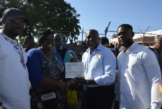 Minister of Labour and Social Security, Hon. Pearnel Charles Jr. (second right), presents Old Shoe Market vendor Cereta Allen (second left), with a cheque valued at $60,000 to assist in replenishing stock lost during a recent fire at the facility in Montego Bay, St. James. Ms. Allen was one of 11 vendors who received cheques from the Ministry on Monday (January 8). Sharing in the moment are (from left) Member of Parliament for Central St. James, Heroy Clarke and Deputy Mayor, Councillor Richard Vernon.