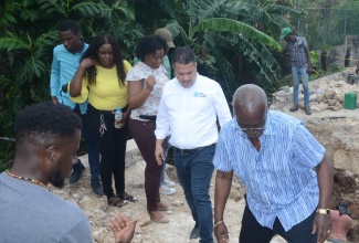 Minister of Local Government and Community Development, Hon. Desmond McKenzie (right), makes his way across a section of a broken bridge in Seville Heights, St. Ann, during a tour on Thursday (January 25). Looking on is Minister without Portfolio in the Ministry of Economic Growth and Job Creation, Senator the Hon. Matthew Samuda (second right), and other representatives from both Ministries and the St. Ann Municipal Corporation.