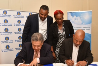 Acting Managing Director, Development Bank of Jamaica (DBJ), David Wan (seated left), and Executive Director, Caribbean Community Climate Change Centre (CCCCC), Dr. Colin Young (seated right), affix their signatures to the Memorandum of Understanding (MoU) formalising the strengthened partnership between the entities, during a ceremony at the ROK Hotel in downtown Kingston on Wednesday (February 21). Witnessing the signing (from left) are: General Manager for DBJ’s Project Management Office, Hugh Grant, and Chair, CCCCC Board of Governors,  Una May Gordon.