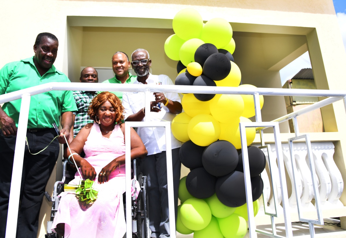 Minister of Local Government and Community Development, Hon. Desmond McKenzie (right), cuts the ribbon to officially hand over a house to recipient, Claudia Green (centre, wheelchair), in Pagee, Port Maria, St. Mary, on Monday (February 12). The unit was provided under the Government’s Indigent Housing Programme. Others (from left) are Member of Parliament, St Mary Western, Robert Montague; Councillor, Port Maria Division, Germaine Smiley; and Port Maria Mayor, Councillor Richard Creary.

