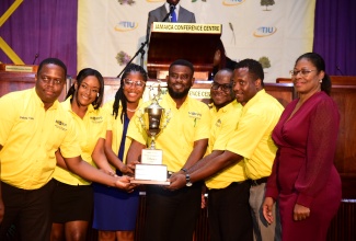 Members of the Ministry of Finance and the Public Service debate team with the Champion Trophy, after winning the second staging of the Public Sector Debate Competition in 2023. Sharing the moment with them is Executive Director, Transformation Implementation Unit (TIU), Maria Thompson Walters (right).

