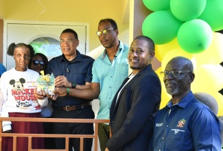 Prime Minister, the Most Hon. Andrew Holness (fourth right), presents burn victim, Adrianna Laing (left) and her father , Adrian Laing (third right) with the keys to their new home in Slipe, St. Elizabeth, on February 21. Also sharing the moment are (from left) Permanent Secretary in the Ministry of Economic Growth and Job Creation, Arlene Williams (back row); Minister of Agriculture, Fisheries and Mining and Member of Parliament for the area, Hon. Floyd Green, and Minister of Local Government and Community Development, Hon. Desmond McKenzie. The home was constructed under the Government’s New Social Housing Programme (NSHP).