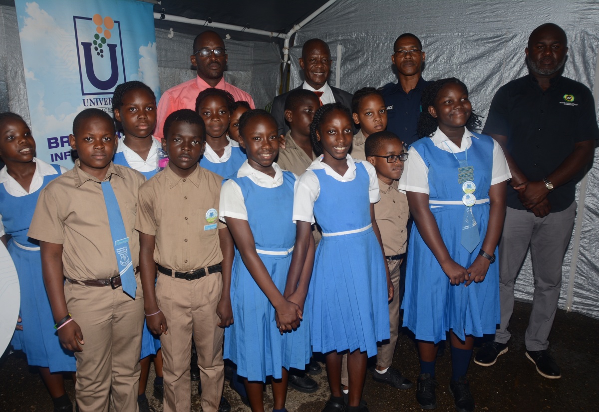 Chief Executive Officer of the Universal Service Fund (USF), Dr. Daniel Dawes (background, second left), joins students of Siloah Primary School and other stakeholders at the launch of Community Wi-Fi in Siloah, St. Elizabeth on Wednesday, March 20.  From left (in background) are Principal of the school, O’Neil Larmond; Sergeant of the Siloah Police Station, Ronnie Wallace; and Parish Manager of the Social Development Commission (SDC), Alric Miller.