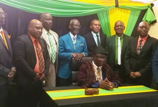 Minister of Local Government and Community Development, Hon. Desmond McKenzie (standing, centre), shares a photo opportunity with re-elected Mayor of Falmouth, Collen Gager (seated), and other councillors of the Trelawny Municipal Corporation, who were sworn into office on Thursday (March 7), at the Municipal Corporation building in Falmouth.