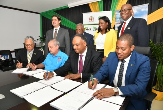 Minister of Agriculture, Fisheries and Mining, Hon. Floyd Green (seated right); Managing Director, Jamaica Social Investment Fund (JSIF), Omar Sweeney (seated second right); Director of Projects, Champion Industrial Equipment and Supplies Limited, Courtney Harford (seated second left) and Chief Executive Officer, Agro-Investment Corporation, Vivion Scully, affix their signatures to documents for the implementation of the Agro-Investment Corporation irrigation Transmission Force Main and Equipping project, at a ceremony at the Ministry of Agriculture, Fisheries and Mining Hope Gardens offices in St. Andrew, on April 11. Witnessing the signing (standing from left) are Programme Lead, The World Bank Group, Emre Ozaltin; Managing Director, Beckford and Dixon Limited, Everad Dixon; Director, Finance and Corporate Planning, National Irrigation Commission, Lillian Smith; and Director of Planning, Projects, Monitoring, Evaluation and Research, National Environment and Planning Agency (NEPA), Ainsworth Carroll.