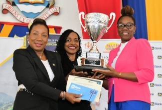 State Minister in the Ministry of Education and Youth, Hon. Marsha Smith (centre), presents Mathematics Teacher of the Year 2024 of Green Pond Primary School, Kamika Ingram (right), with a trophy at the Mathematics Teacher of the Year and Jamaican Mathematical Olympiad (JMO) awards ceremony held on April 15 at the University of the West Indies (UWI), Mona campus, in Kingston. Manager, Public Sector Engagement, Jamaica National (JN) Bank, Sandra Jones, also hands over a cheque to Ms. Ingram.

