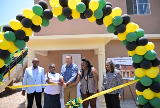 Prime Minister, the Most Hon. Andrew Holness (centre), cuts the ribbon symbolising the formal handover of two three-bedroom units under the New Social Housing Programme (NSHP) to beneficiaries, Claudia Ford (second left), and Tracy Ann Benjamin (second right). The mother-and-daughter duo were presented with their keys during a ribbon-cutting ceremony in Maxfield Park, St. Andrew, on Friday (April 12). Sharing the moment are (from left) Councillor, Maxfield Park Division, Dennis Gordon, and Chair, Oversight Committee, NSHP, Judith Robb Walters.