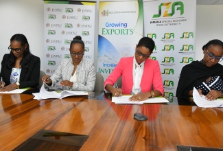 Chief Executive Officer of the Jamaica Special Economic Zone Authority (JSEZA), Kelli-Dawn Hamilton (second right) and Acting Vice President, Investment and Linkages, Jamaica Promotions Corporation (JAMPRO), Gail Barrett (left), sign a Memorandum of Understanding (MOU) to strengthen cooperation between the entities, while President of Jamaica Promotions Corporation (JAMPRO), Shullette Cox (second left) and Senior Director, Business Partners and Support Services, JSEZA, Licia Grant, prepare to affix their signatures. The agreement, which was signed on Wednesday (April 3) at JAMPRO’s New Kingston offices, will enhance coordination of investment promotion and marketing, improve information sharing and support export and investor relations. This strengthened cooperation between JAMPRO and the JSEZA is important for the effective implementation of the special economic zone regime and Jamaica’s integration into global supply and value chains, in alignment with the vision of the island as a global logistics hub.