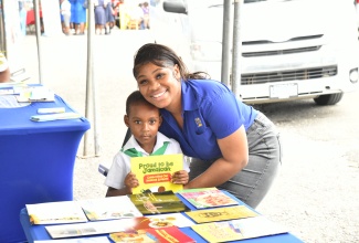  Special Projects Officer, Jamaica Information Service (JIS), Romona Geohaghan, presents a copy of the JIS publication ‘Proud To Be Jamaican’ to little Khajarie Grant, who visited the JIS booth during the St. Mary 4-H Clubs’ Parish Achievement Expo, held recently at the St. Mary High School.