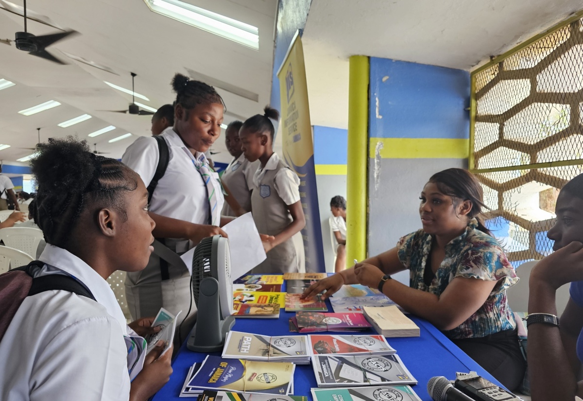 Jamaica Information Service (JIS) Special Projects Officer, Romona Geohaghan, interacts with fifth-form students at Vauxhall High School, Rayana Thompson (left, seated) and Fantasia Ryman (second left) at the institution’s Career Day on April 18.