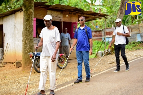 Visually impaired resident of Mt. Providence Square in Clarendon, Denvill Dinnal (left), leads members of the May Pen chapter of the Jamaica Society for the Blind on a walk in his community, shortly after receiving his new cane from Minister without Portfolio in the Ministry of Economic Growth and Job Creation with responsibility for Works, and Member of Parliament for Clarendon North Central, Hon. Robert Morgan on Labour Day (May 23). The members are (from second left) Denzel Thompson; and Ovestra King.
