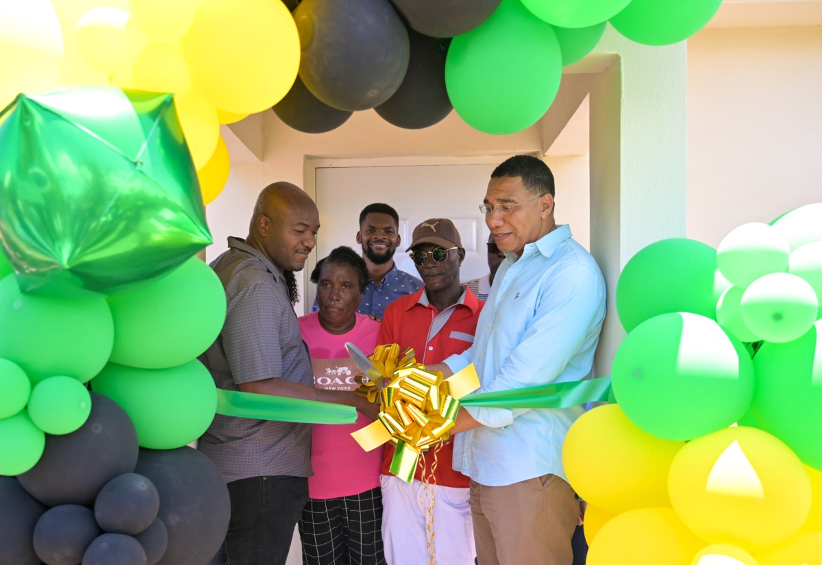 Prime Minister, the Most Hon. Andrew Holness (right), cuts the ribbon to handover a home under the New Social Housing Programme (NSHP), to Gerald McKenzie (second right) in Race Course, Clarendon on Friday (May 24). Others sharing in the occasion from left are: Member of Parliament for Clarendon South Western, Lothan Cousins, and Mr. McKenzie’s spouse, Verna Redhi.