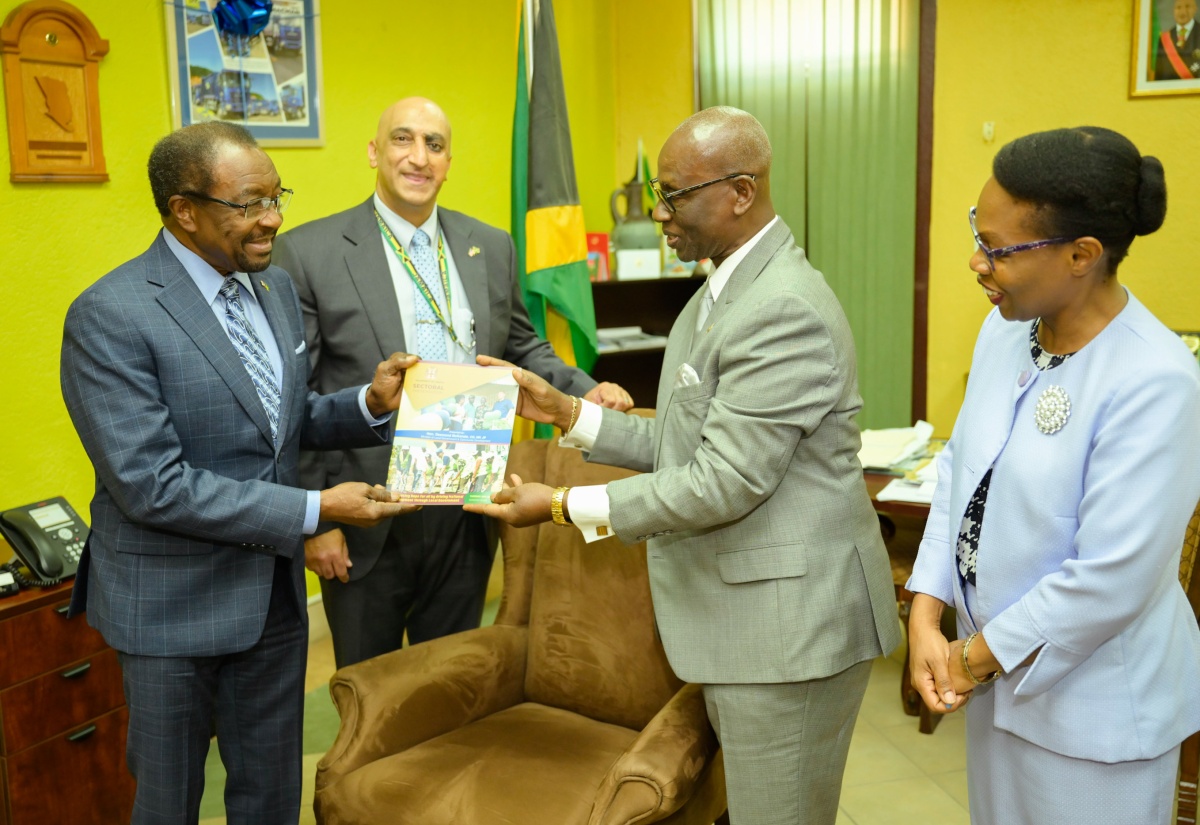 Minister of Local Government and Community Development, Hon. Desmond McKenzie (second right), presents United States Ambassador to Jamaica, His Excellency Nick Perry (left) with a copy of his sectoral presentation when the Ambassador visited the Minister’s Hagley Park Road offices in Kingston on May 30. Sharing in the moment are Country Representative for the United States Agency for International Development (USAID), Dr. Jaidev Singh, and Permanent Secretary in the Ministry, Marsha Henry-Martin.