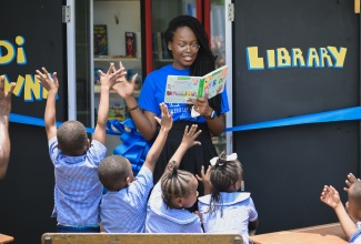 Volunteer, Jodeane Bailey reads a book to students at the opening of the sixth ‘Di Corna Library’ in Cassava Piece, St. Andrew, on May 7, which was observed as Read Across Jamaica Day.  Di Corna Library is a sustainable community initiative aimed at providing a variety of books and school resources to under-served communities. Under the initiative, conceptualised by education specialist Rachel McDonald, old refrigerators are repurposed into book cupboards to store books that children and adults can borrow, read and return.


