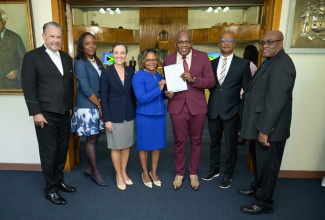 Minister Without Portfolio in the Office of the Prime Minister with Responsibility for Skills and Digital Transformation, Senator Dr. the Hon. Dana Morris Dixon (centre), presents Opposition Senator, Dr. Floyd Morris (third right) with a copy of his birth certificate in Braille during a brief ceremony before the start of the sitting of the Senate at Gordon House on Friday (May 10). Others sharing the moment (from left) are President of the Senate, Senator Tom Tavares-Finson; Clerk to the Houses of Parliament, Colleen Lowe; Minister of Foreign Affairs and Foreign Trade, Senator the Hon. Kamina Johnson Smith; Opposition Senator, Peter Bunting; and Acting Chief Executive Officer, Registrar General