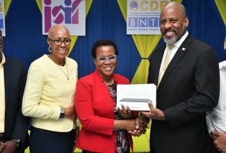 Education and Youth Minister, Hon. Fayval Williams (left), observes as Chairman of the Board, Jamaica Social Investment Fund (JSIF), Dr. Wayne Henry (right), hands over a tablet computer to Director of The Mico University College Child Assessment and Research in Education (CARE) Centre, Sharon Anderson-Morgan. The event was the Basic Needs Trust Fund (BNTF) capacity-building for special education contract signing ceremony on May 9, at The Mico University College in Kingston.