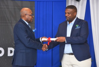 Minister of Tourism, Hon. Edmund Bartlett- (left) makes a presentation to Founder, Caribbean Front Desk and winner of the inaugural Tourism Innovation Incubator pitch event, Dr. Duane Chambers at the initiative’s closing ceremony last year at the Summit in Kingston.