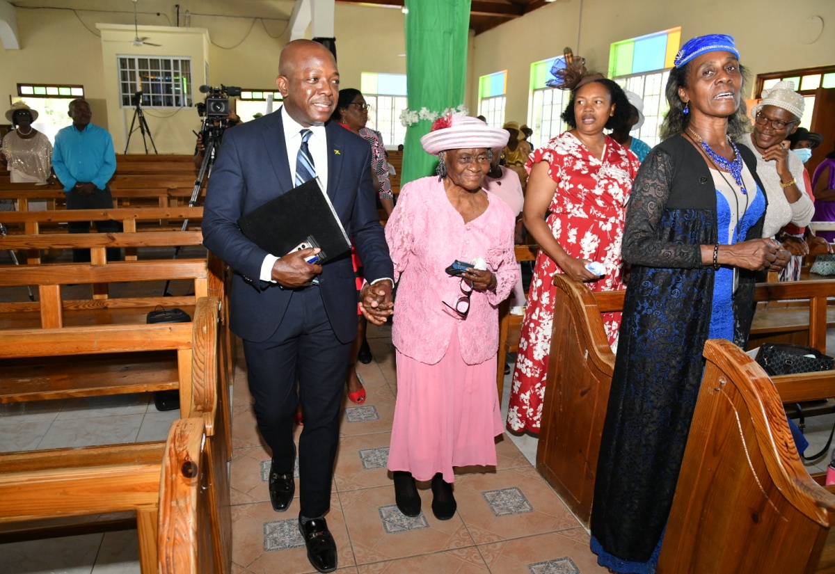 Minister of Labour and Social Security, Hon. Pearnel Charles Jr. (left), escorts 101-year-old Keturah Headley-Campbell of Waterworks in Westmoreland, to her seat at the National Church Service to mark the 58th Anniversary of the National Insurance Scheme, held on Sunday, May 26, at the Torrington Wesleyan Holiness Church, in the parish.
