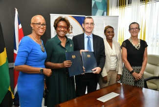 Permanent Secretary, Ministry of National Security, Ambassador Alison Stone Roofe (second left) and United Kingdom (UK) Development Representative for Jamaica, Oliver Blake (centre), display the signed Memorandum of Understanding (MOU) for the six-year Violence Prevention Partnership between the Government of Jamaica and the UK, at the offices of the Ministry of National Security in Kingston. They are flanked by (from left), Minister of Education and Youth, Hon. Fayval Williams; State Minister, Ministry of National Security, Hon. Juliet Cuthbert-Flynn; and British High Commissioner to Jamaica, Her Excellency Judith Slater.