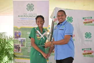 Minister of Agriculture, Fisheries and Mining, Hon. Floyd Green, hands over a trophy to the newly crowned Jamaica 4-H Clubs 2024 Female Youth Ambassador of the Year, Deneila Wright,  at the National Achievement Day, on May 10. Ms. Wright is a student at Knox College in Clarendon.