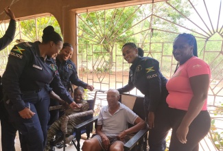 Head of the Guanaboa Vale Police, Sergeant Navelette Davis-Leachman (left); office attendant at the station, Glacier Maxwell (right), along with other officers from the station, interact with resident of the St. Catherine-based Rock of Hope Residential Manor, James Mitchell (seated), on Labour Day (May 2023).

