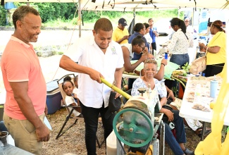 Minister of Agriculture, Fisheries and Mining, Hon. Floyd Green (right), tries out a cane juicer during the Hanover Agricultural Show held at Lord’s Playfield in Lucea on Friday, (May 24). Looking on is Quantity Surveyor and farmer, Paul Trench. 