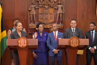 Minister of Legal and Constitutional Affairs, Hon. Marlene Malahoo Forte (at podium), addresses Wednesday’s (May 22) post-Cabinet press briefing at Jamaica House. With the Minister are some members of the Constitutional Reform Committee (CRC) (from left) Civil Society Representative, Dr. Nadeen Spence (partly hidden); Chairman of the Jamaica Umbrella Group of Churches, Dr. Elaine McCarthy; CRC Co-Chair, Ambassador Rocky Meade; Attorney General, Dr. Derrick McKoy; and Youth Advisor, Sujae Boswell.