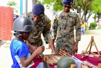 Lieutenant Kyle-Anthony Mundell (centre) of the Jamaica Defence Force, explains the roles and functions of combat engineers to a curious young patron at the Kingston and St. Andrew Municipal Corporation (KSAMC) All Hazards Expo and Emergency Cook-Off, held at the St. William Grant Park, downtown Kingston on Friday June 21. Looking on is Lieutenant Rojae Pickersgill.