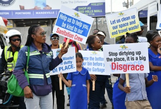 MPM Waste Management Limited staff are joined by students in displaying signs promoting environmental responsibility during an environmental awareness march from Red Hills Mall to Swallowfield Primary in Kingston on June 4. The event, held in observance of National Environmental Awareness Week from June 1-8, involved Swallowfield Primary School students, Social Development Commission (SDC) representatives, and White Hall Community Development Committee (CDC) members.