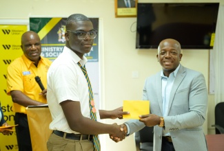 Minister of Labour and Social Security, Hon. Pearnel Charles Jr., presents an academic grant to Roger Clarke High School student Michael Blake, during a handover ceremony, held at the St. Elizabeth Technical High School in Santa Cruz, on June 5. The 22 grants to students in St. Elizabeth  were provided by Jamaican farm workers at Gebbers Farms in Washington, United States. 