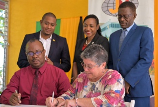 Papine High School Principal, Leighton Christie (seated left), looks on as General Manager, Jamaica Bauxite Institute (JBI), Yolanda Drakapoulos, signs a Memorandum of Understanding (MOU) for the use of a greenhouse owned by the JBI for the advancement of the school’s agriculture programme. The ceremony was held on June 14 at the JBI’s offices in St. Andrew where the greenhouse is situated. Looking on are (from left) Minister of Agriculture, Fisheries and Mining, Hon. Floyd Green; State Minister in the Ministry of Education and Youth, Hon. Marsha Smith; and Board Chair of the Papine High School, Dr. Noel Watson.
