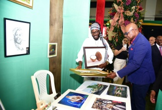 Tourism Minister, Hon. Edmund Bartlett (right), admires a canvas painting by artist Delroy Millwood (left). Occasion was the opening of the two-day Christmas in July trade show on July 11, at the National Arena.