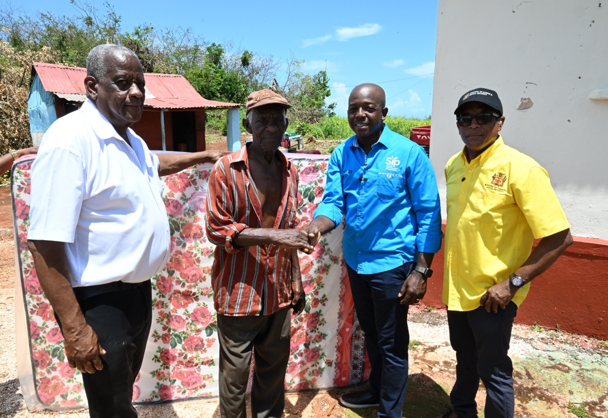 Minister of Labour and Social Security, Hon. Pearnel Charles Jr. (second right) hands over a mattress to resident of Tryall, Nascius Powell (second left), during a tour of communities in southern St. Elizabeth on July 12. Looking on (from left) are State Minister in the Ministry of Agriculture, Fisheries and Mining, Hon. Franklin Witter and Minister of State in the Ministry of Labour and Social Security, Dr. the Hon. Norman Dunn.