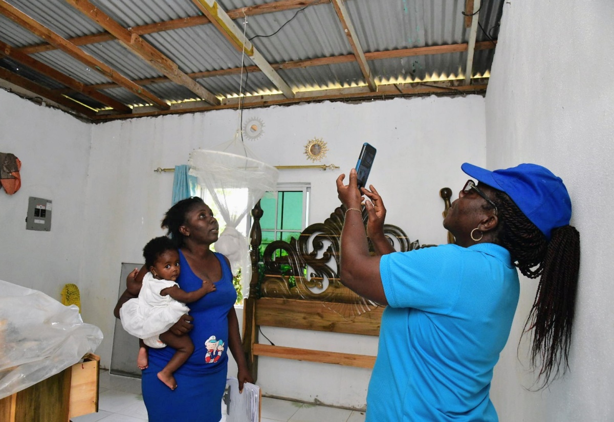 Social Worker, Ministry of Labour and Social Security, Clurdine Powell Harrison, uses a mobile phone to capture images highlighting damage to Cameka Chamberlin's residence in Mitchell Town, during the passage of Hurricane Beryl on July 3. Occasion was a visit to the community in Clarendon on July 10 by teams from the Ministry to assess the damage and provide relief items to the affected residents.

