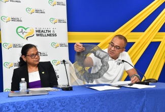 Minister of Health and Wellness, Dr. the Hon. Christopher Tufton (right), displays a mosquito drum cover during a press conference at the Ministry’s New Kingston offices on July 18. At left is Chief Medical Officer in the Ministry, Dr. Jacquiline Bisasor-McKenzie. The press conference provided an update on the state of dengue and the Government’s Enhanced Vector Control Programme, as well as the post-hurricane plan for the public health system.