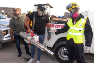 Minister of Health and Wellness, Dr. the Hon. Christopher Tufton (centre), tests a handheld fogging machine while in Rocky Point, Clarendon, on July 25. Pictured at left is Deputy Chairman for the Southern Regional Health Authority (SRHA), Michael Stern, while a vector-control worker is at right.