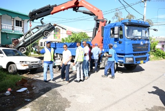 Executive Director of the NSWMA, Audley Gordon (left), in discussion with Minister of Legal and Constitutional Affairs and Member of Parliament for St. James West Central, Hon. Marlene Malahoo Forte (second left), as the entity removes a derelict vehicle from a section of Catherine Hall, during the launch of the Bulky Waste and Derelict Vehicle Removal Programme in St. James on Thursday, August 8. Also at the site are (from third left) Mayor of Montego Bay and Chairman of the St. James Municipal Corporation, Councillor Richard Vernon; Regional Operations Manager of WPM Waste Management Limited, Edward Muir,  and other NSWMA personnel

