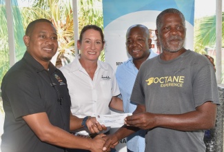 Minister of Agriculture, Fisheries and Mining, Hon. Floyd Green (left), presents a cheque, valued $25,000, to net fisher George Daley (right), during a presentation ceremony at the Caribbean Coastal Area Management (C-CAM) Foundation Field Station in Salt River, Clarendon, on Thursday (August 22). Sharing the moment are (from left) Executive Director, Sandals Foundation, Heidi Clarke; and Minister of Labour and Social Security and Member of Parliament for Clarendon South Eastern, Hon. Pearnel Charles Jr.