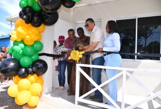 Prime Minister, the Most Hon. Andrew Holness (second right), and Permanent Secretary in the Ministry of Economic Growth and Job Creation, Arlene Williams (right), cut a ribbon during Friday’s (September 6) handover ceremony for a new housing unit at Lot 129 Callaloo Mews, St. Andrew Western, which was developed under the New Social Housing Programme (NSHP). They are joined by Member of Parliament for the constituency, Anthony Hylton (second left), NSHP beneficiary and recipient of the unit, Karen Francis (centre), and her granddaughter, Trishanna Carter (left).

