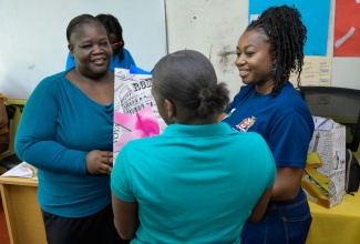 Acting Director, Community Liaison Unit, Bureau of Gender Affairs (BGA), Nardia McClaren (right), presents a gift to a resident of the Homestead Residential Facility, while Health and Social Care Supervisor at the facility, Latoya Brown, looks on.  Members of the BGA visited the home in St. Andrew on Friday (October 11) to celebrate with the residents on International Day of the Girl Child under the theme 'Girls' Vision for the Future'.