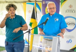 Minister of Justice, Hon. Delroy Chuck (right), delivers the keynote address at the St. Mary leg of the Legal Aid Council’s justice fair for persons with disabilities, at the Claude Stuart Park in Port Maria on October 23. At left is interpreter, Toni Aiken.

