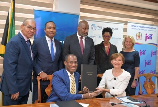 Minister of Finance and the Public Service, Dr. the Hon. Nigel Clarke (left, seated), and World Bank Country Director for Latin America and the Caribbean (LAC), Lilia Burunciuc (right, seated), display the signed US$12-million loan agreement for the Kingston Waterfront Improvement Project. Other participants in the proceedings are (from left, standing) General Manager, Finance and Procurement, Jamaica Social Investment Fund (JSIF), Orville Hill; General Manager, Urban Development Corporation (UDC), Robert Honeyghan; JSIF Chairman, Dr. Wayne Henry; Chief Technical Director, Office of the Prime Minister, Shereika Hemmings Allison, and Operations Manager, World Bank, Gail Richardson.

